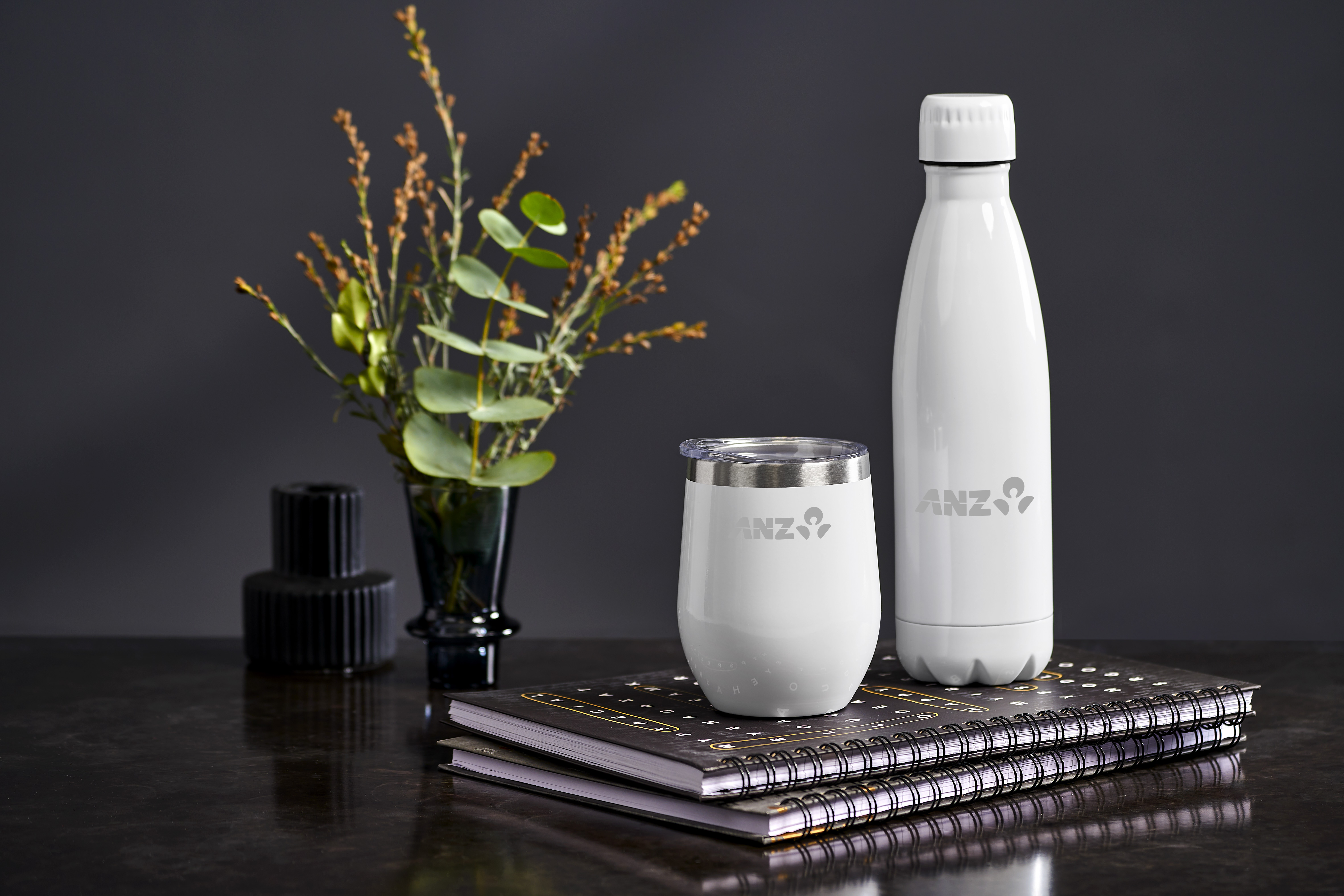 Branded white bottle and tumbler with notebooks and a floral arrangement